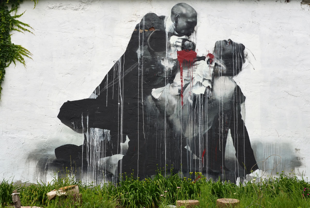 Wall Therapy mural in Rochester, on the side of a building, in black and white, what looks like one man murdering another, the blood is red which is the only colour in the painting