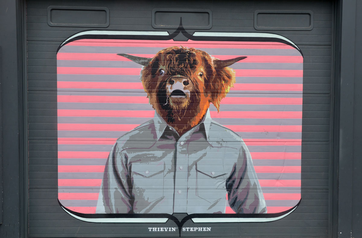 Thievin Stephen is the title, Wall Therapy mural in Rochester, on the side of a building, a man's torso in a light grey shirt, but with a cow head, pink background