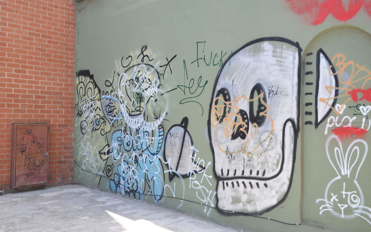 Graffiti on a cement wall. A man's face, a skull and a rabbit, all scrawled. 