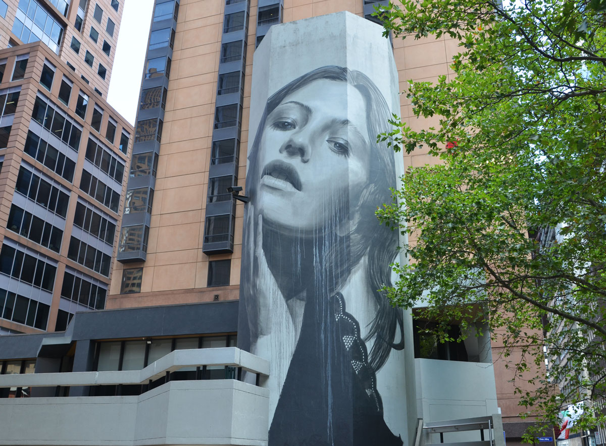 Large mural of a woman's head on a building, black and white and gray, one hand is touching her cheek. 