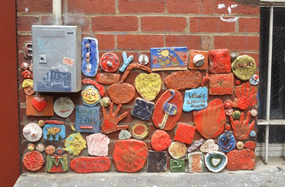 many clay pieces, a hand, some with words, attached to a wall, part of a Legacy project for ANZAC commemoration