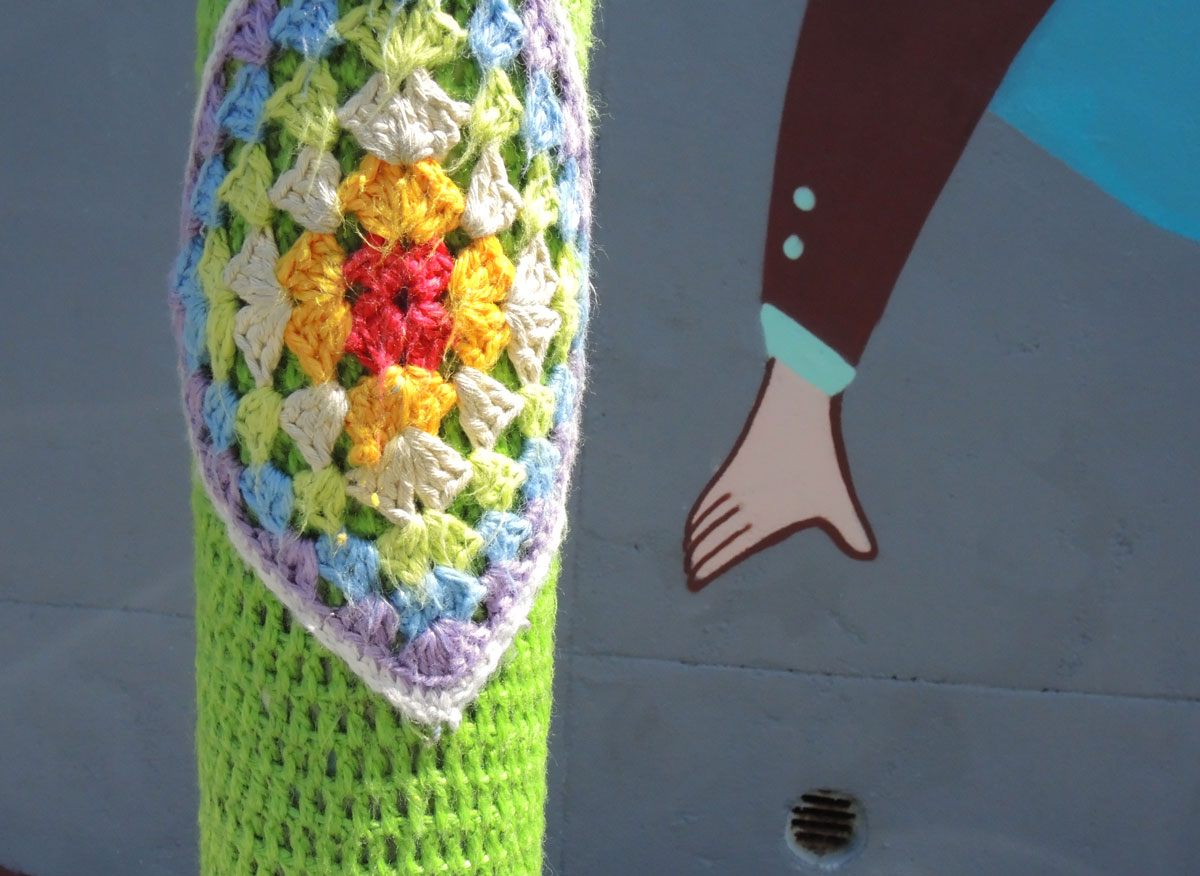 pole wrapped in colourful yarn crocheted in square pattern, laid on point, with green crochet yarn around the diamonds. 