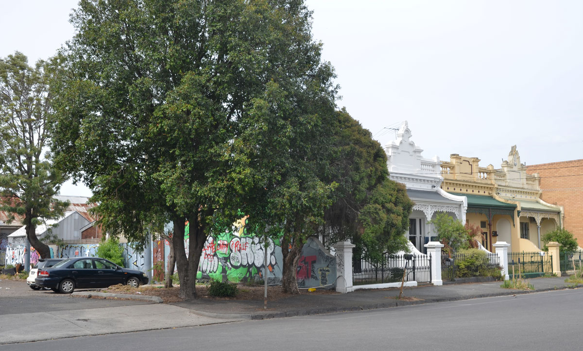 a row of terrace houses in Brunswick Melbourne with a parking lot at the left side. The side of the house closest to the car park has a mural painted on it.