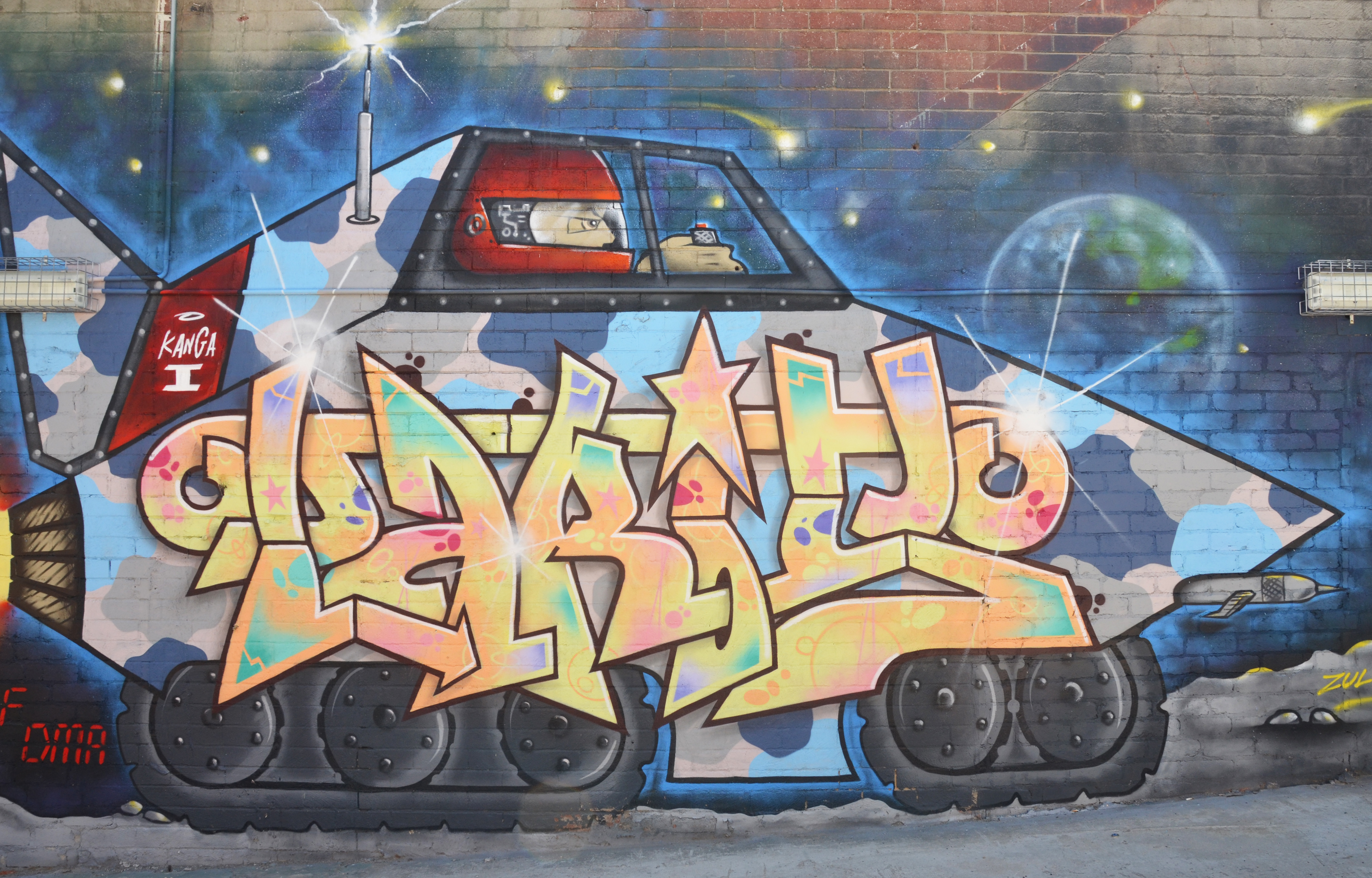 Street art painting of text within a large armed vehicle, large black tires