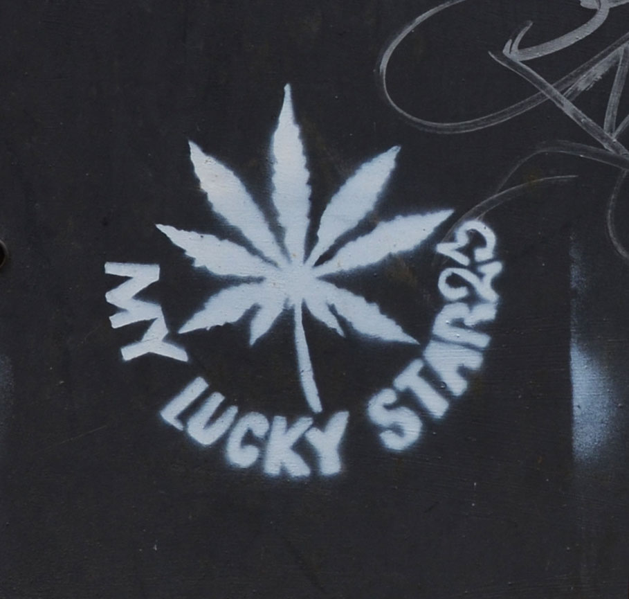white stencil on black of leaf from marijuana plant with the words my lucky star23 written aroud it. On black background