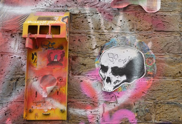 paste up of a skull, old mailbox broken, spray painted yellow and stickers on it 
