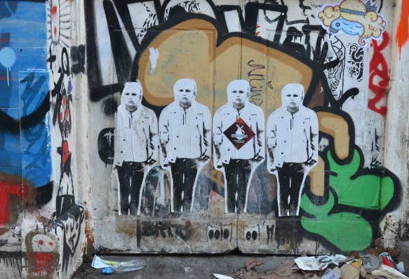paste up of four men standing in a line, shoulder to shoulder, on a background of graffiti tags. 