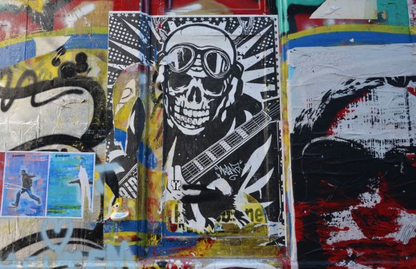 street art of a man with skull face, helmet and googles on his forehead, ammo belt across his chest. 