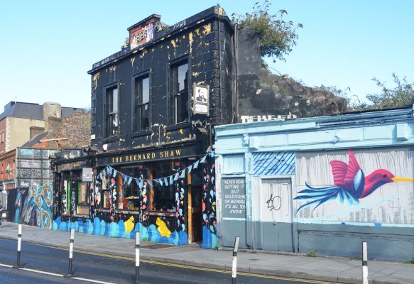an old black building, the Bernard Shaw pub, built 1895, with street art on either side of it. 