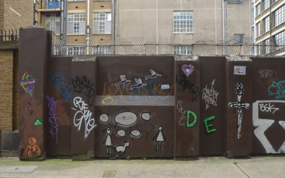 brown wall with barbed wire across the top, covered with graffiti