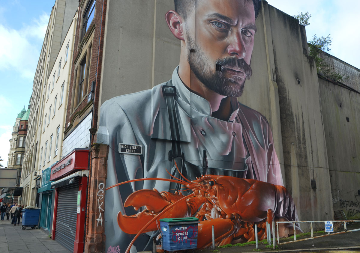 very marge mural of a man with moustache and small beard and wearing a chef's shirt is holding a large lobster