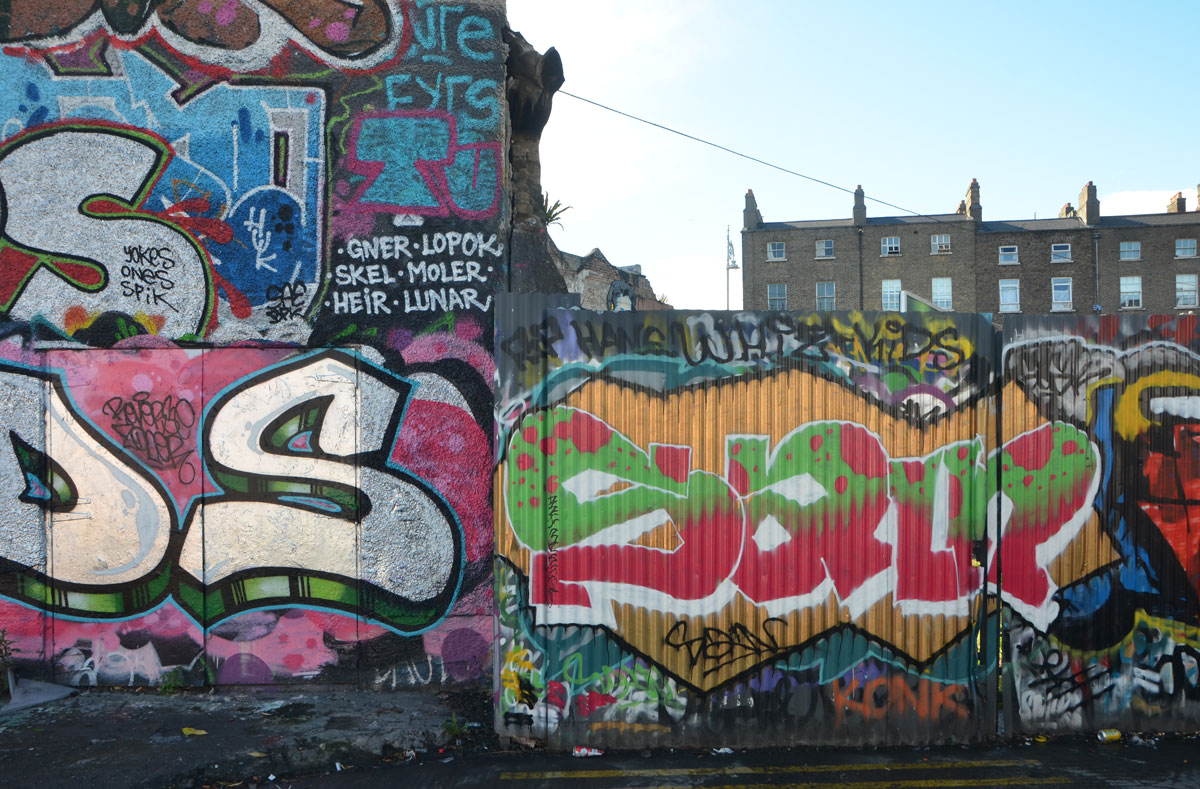 graffiti and street art on building and fence, with brick rowhouses behind, Dublin