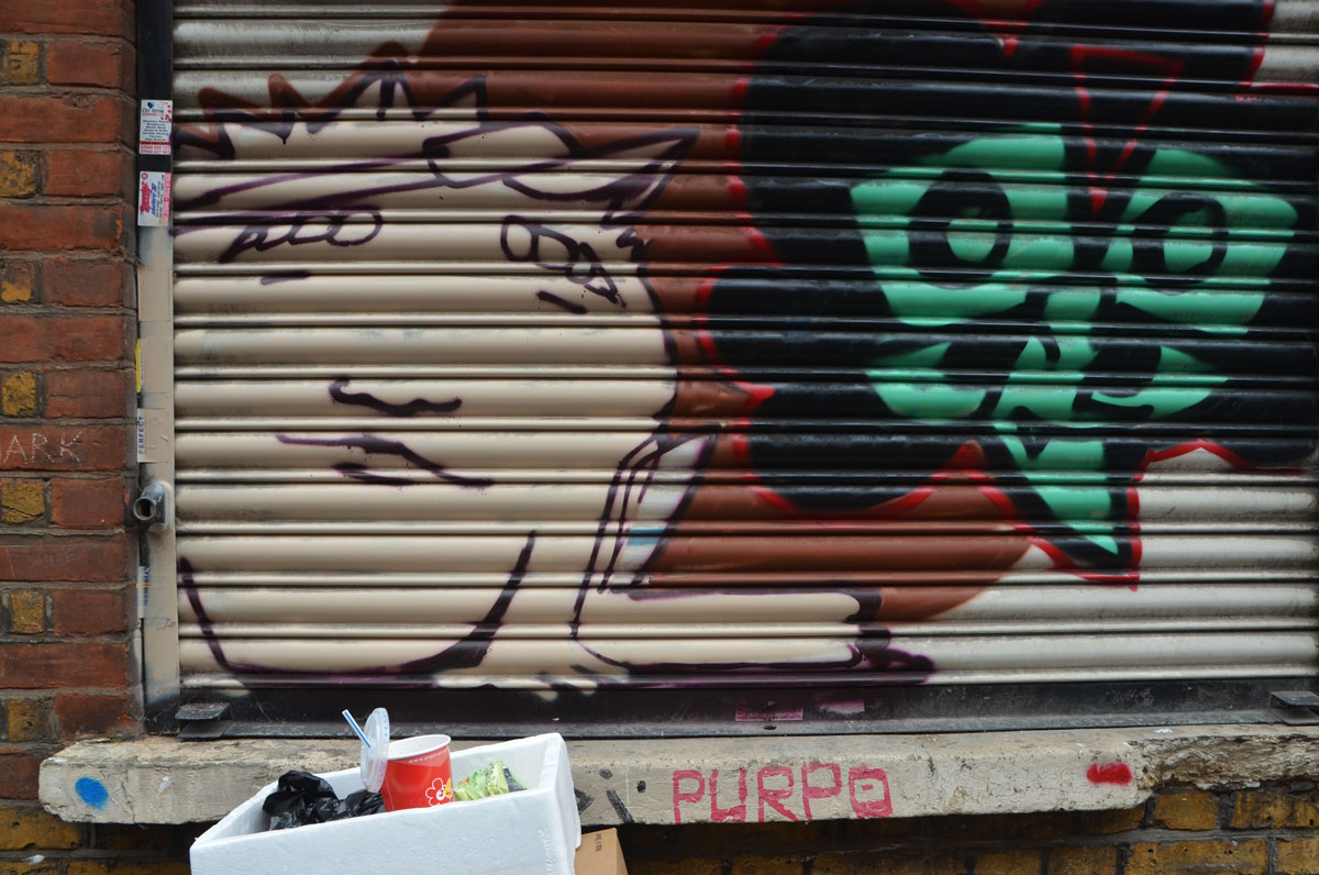 two street art faces painted on a metal covering over a shop window. One is man's face in beige with brown hair and the other is a stylized face in green with black hair