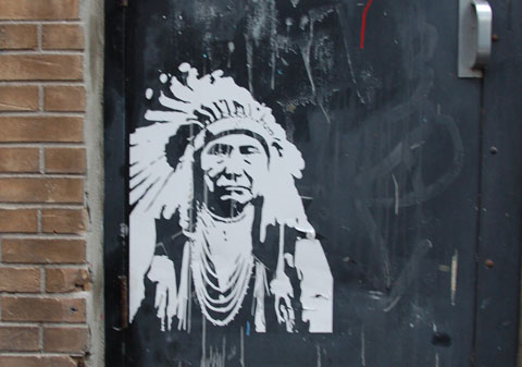 a white stencil of an older Indian (first nations) man in a feather head dress. A stereotypical picture of Indian chief from old pictures 