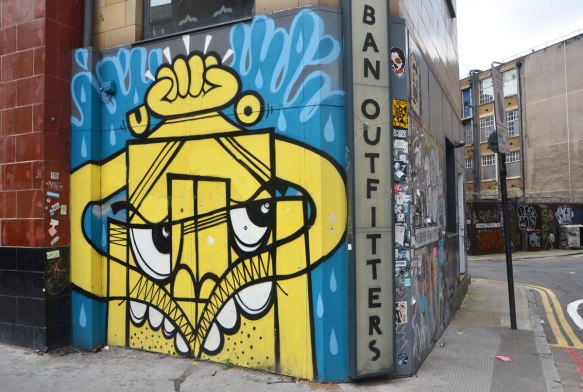 mural in yellow and blue on exterior wall of urban outfitters in Shoreditch London, abstract face with white eyes and teeth 