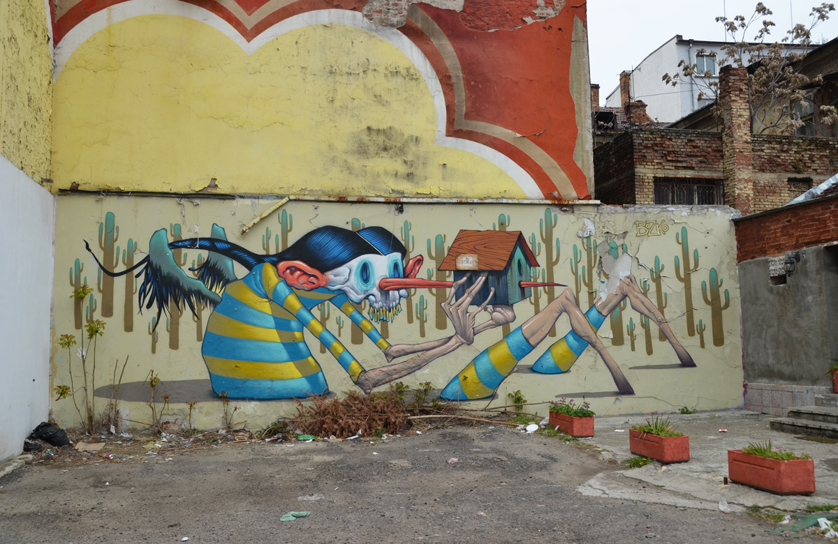 mural by Bozko on a wall in Sofia, a wooden person-like creatire with a long nose is holding a bird house, his nose pierces the bird house. 