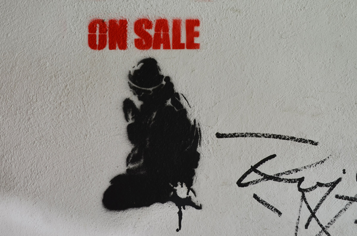 stencil, black, seated person with red block capital letters above the head that say on sale