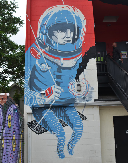 an astronaut dressed in blue sitting on a kids swing, mural, two storeys high, helmet, 