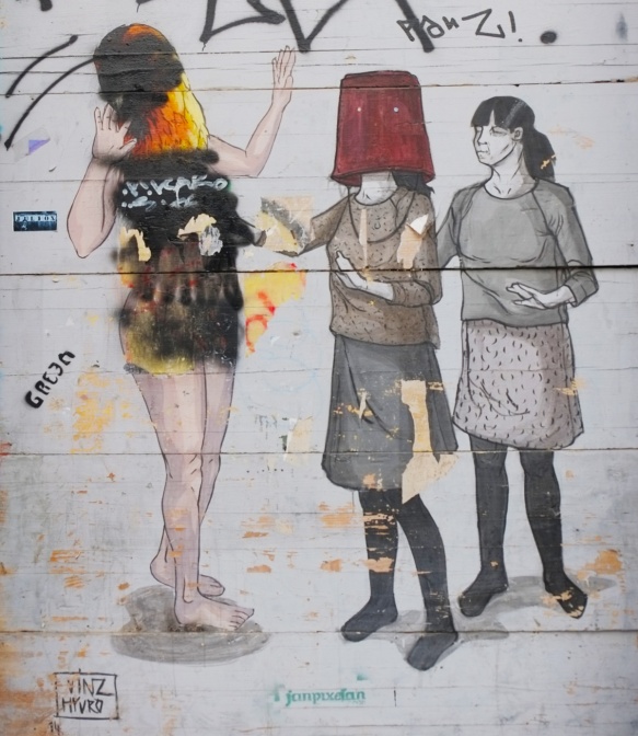 mural on a wall, three women, one in the middle has a red bucket over her head, she is reaching out to the one on the left who has been defaced (port painting). by vynz and hyuro. 
