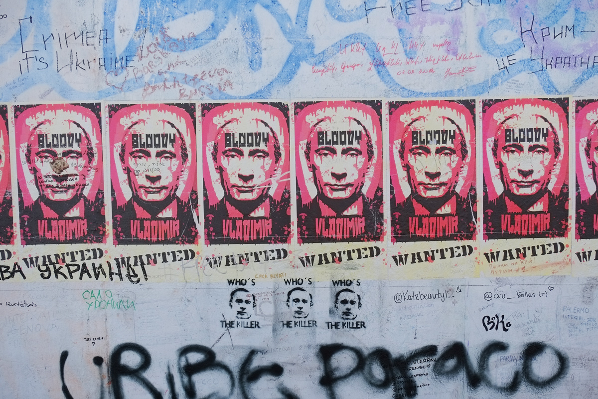 part of a mural on Berlin Wall, Eastside gallery - posters with the face of Putin, Russin leader, with words, Bloody Vladimir, wanted poster 