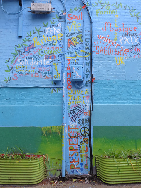 street art mural in an alley, shape of a tree but filled in with words in different colours, words shuch as passion, communate, respect, fierte, English, French and Spanish words. 