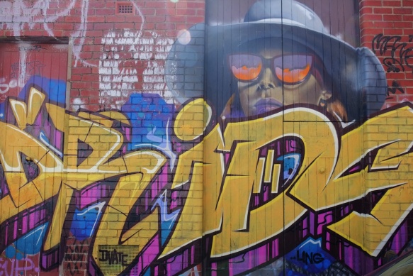 gold letter text street art with a picture of a woman in broad rimmed hat and purple and orange sunglasses 