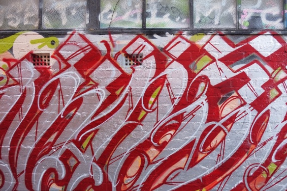 red and silver graffiti on a wall underneath a row of windows with frosted glass 