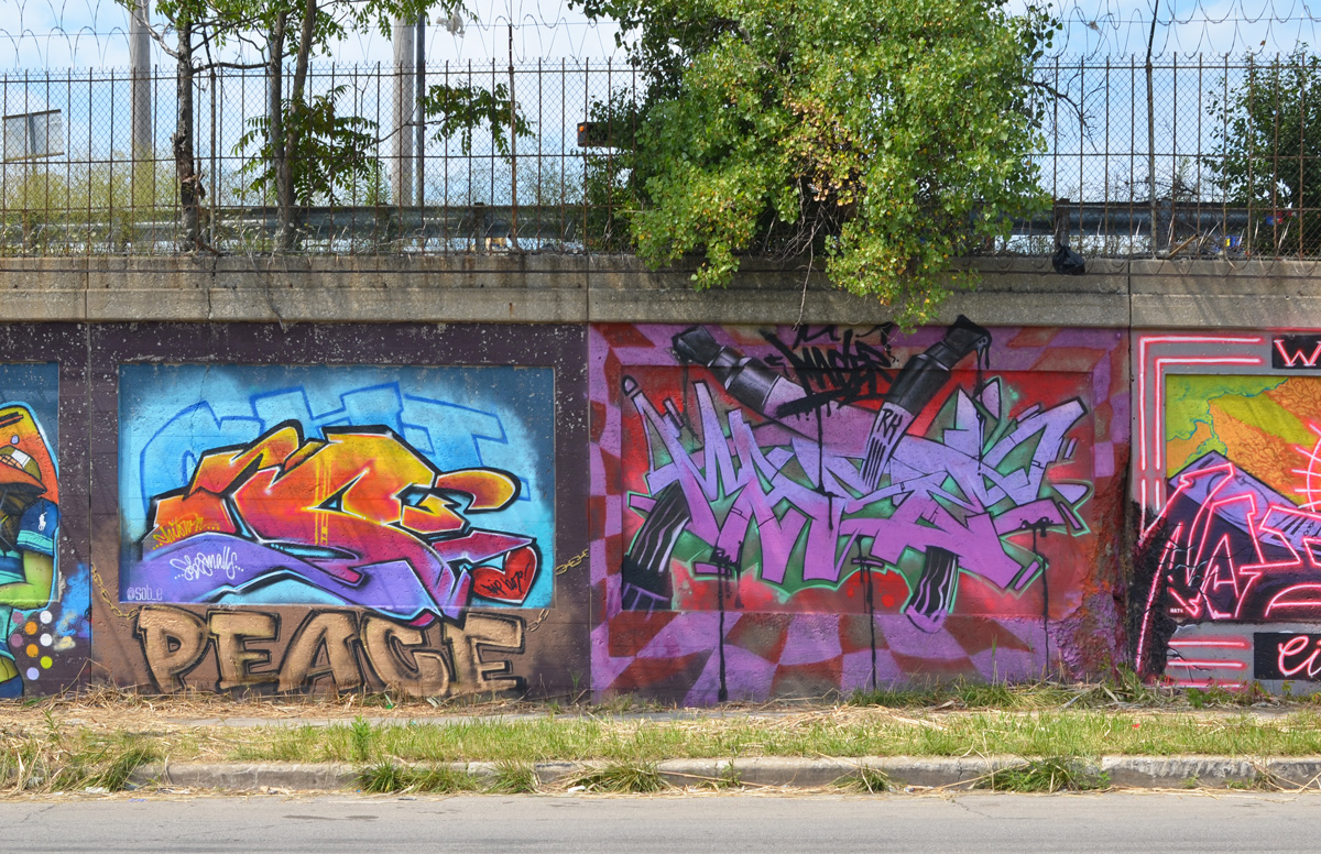 two murals on a wall beside a street, one has the word peace 