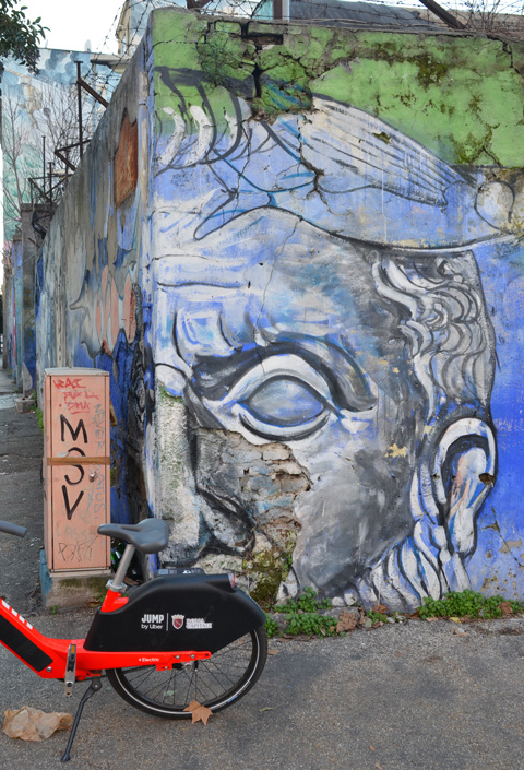 corner of wall, painted face, mural on both sides of the corner, rental bike, jump, parked in front 