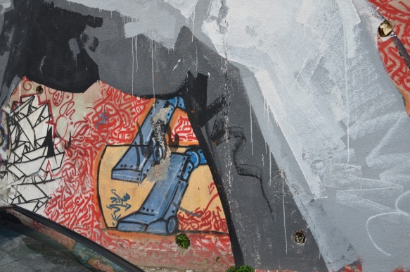 part of a large mural of a grey man covers an older street art painting of a blue robot on background made with red Arabic calligraphy