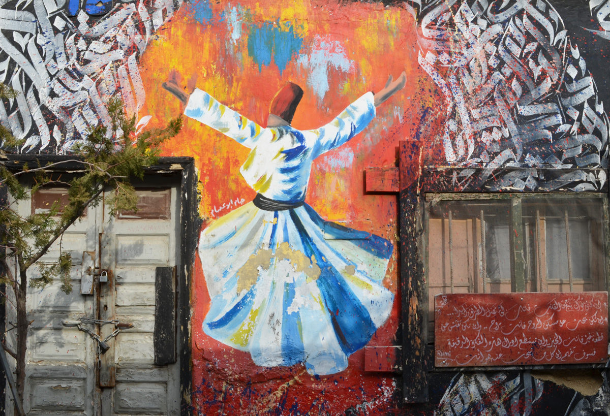 between two shuttered windows, a street art painting surrounded by white Arabic calligraphy on red, in the middle is the back of a dancer with red hat and long white robe tied at the waist, long skirt that twirls outward as dancer moves