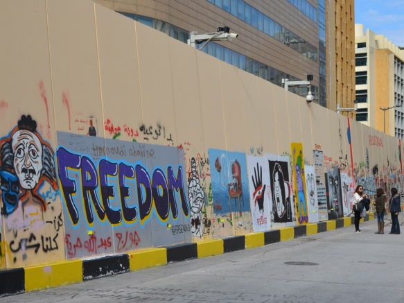 looking along a wall full of protest street art including a large word freedom