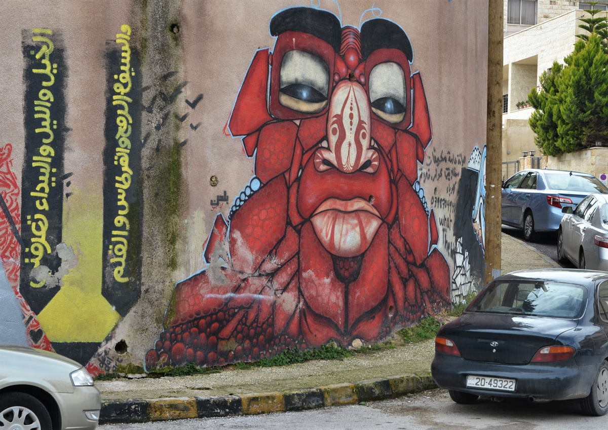 two graffiti pieces, on the left an Arabic verse written vertically and on the right, a red monter head and shoulders, 
