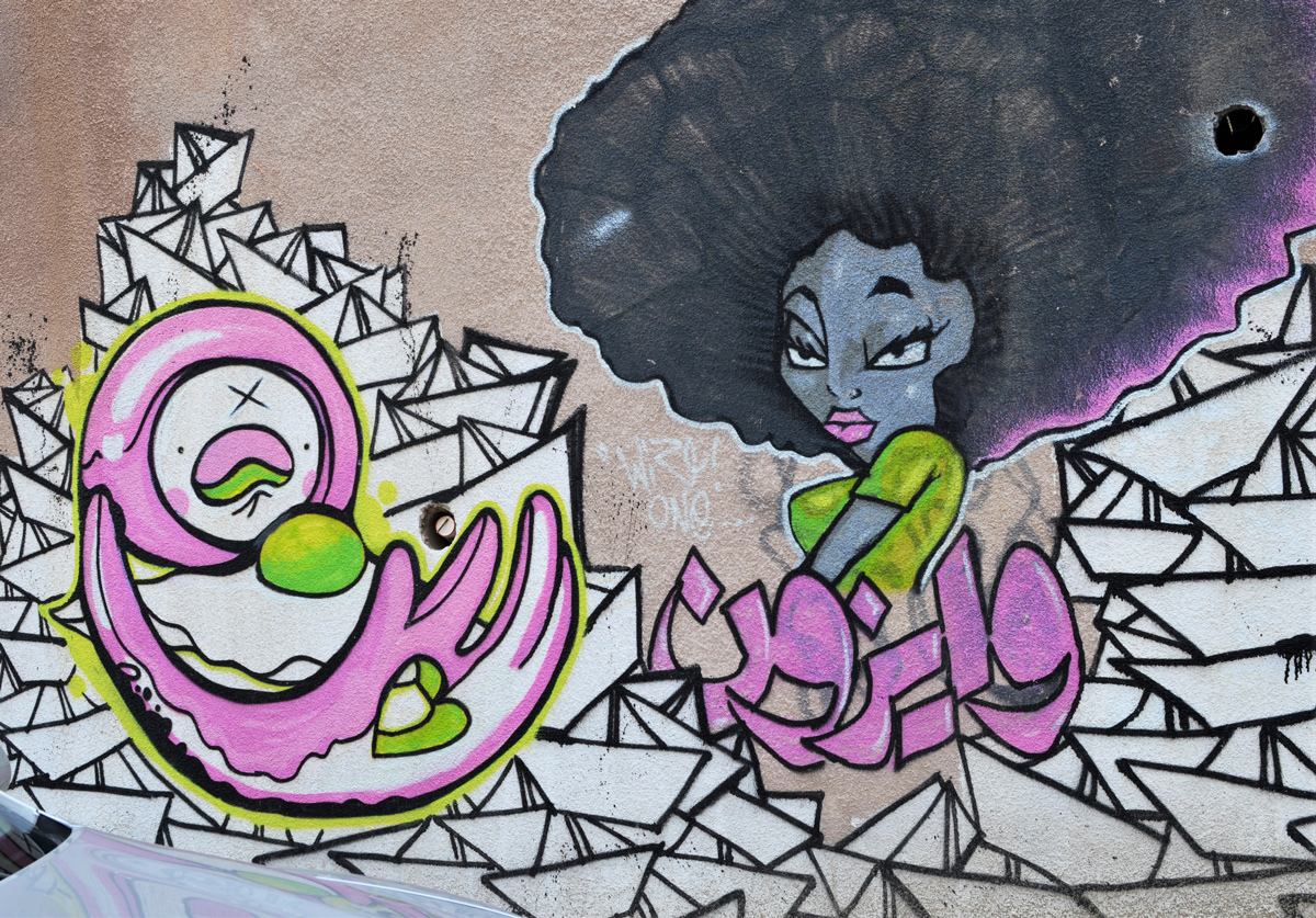 street art on a wall in Amman, a woman with big afro hair by many white paper boats and a character in pink and white, curved arms stylized face