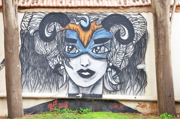 a painting by Zein of a woman's head, wearing blue eye mask, with curved horns