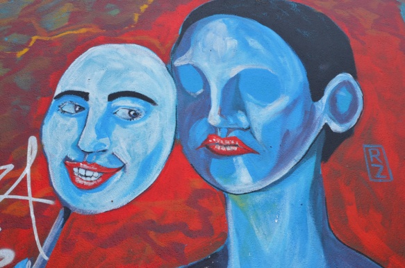street art painting of a blue person holding a blue mask on a stick in front of her face.  Mask is a happy face, real face is blank. 