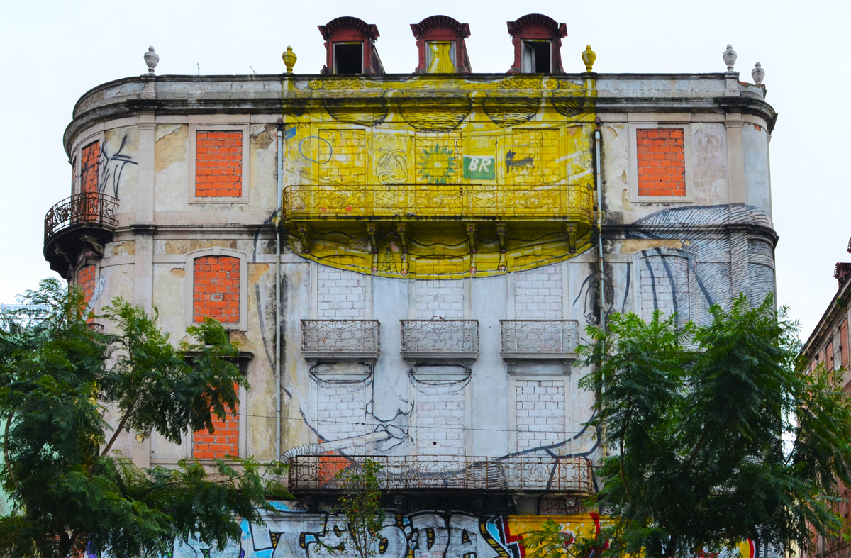 large mural of a white face, male, wearing large gold crown, on three storey Lisboa building
