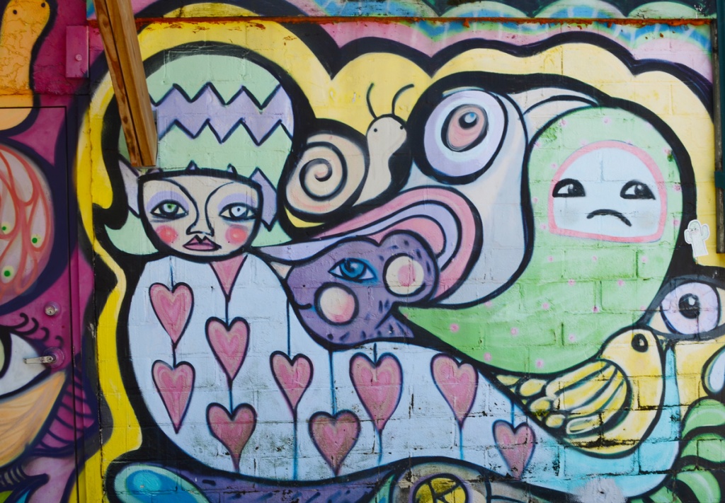 mural in an alley of a female figure dressed in a red heart covered dress.  There is a large snail on her lap