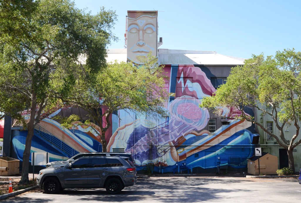 large mural by parking lot in St. Petersburg, called Time to think, painted by Derek Donnelly and Sebastian Coolidge, a man in a shirt and green tie, upper body only, is opening his middle to release a jellyfish like structure
