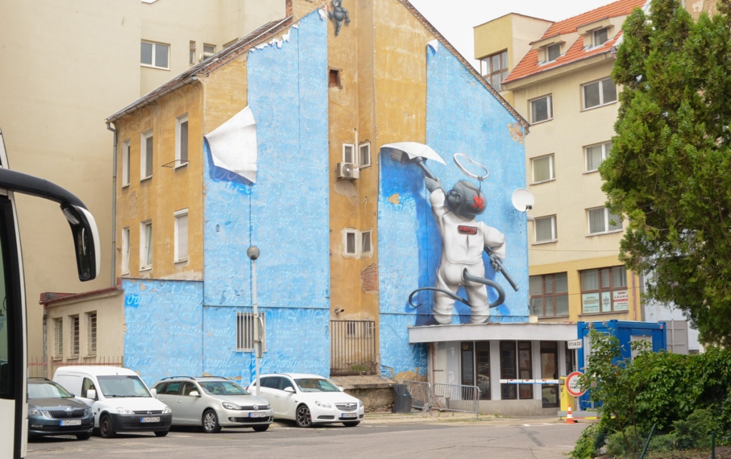 mural, a character in a white puffy suit is using forced air to hang blue wall paper.  paper has pattern of words ego and vanity in white