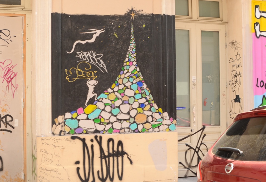street art painting of a white silhouette naked man climbing a mountain of multi coloured rocks, with a star at the very top