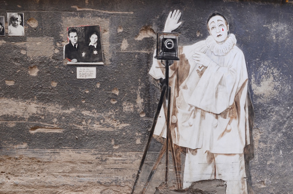 street art, three black and white photos of people who used to live in the courtyard.  A large artwork of Marcel Marceau in white clown mime clothes, a red tear painted on his face, standing beside a vintage box camera on a tripod 