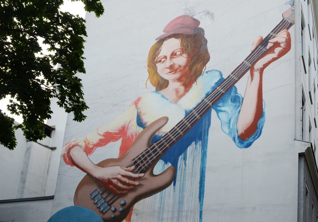 a woman with a red cap on her head is playing an electric guitar, in a mural on the side of a school in Vienna. 