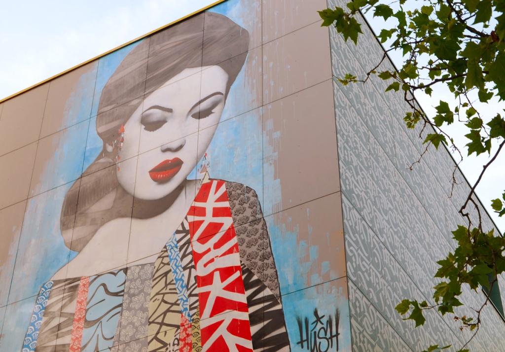 mural by hush portrait of a Japanese woman with bright red lipstick, eyes looking town, clothing made of strips of Japanese print fabric, dark black hair, 