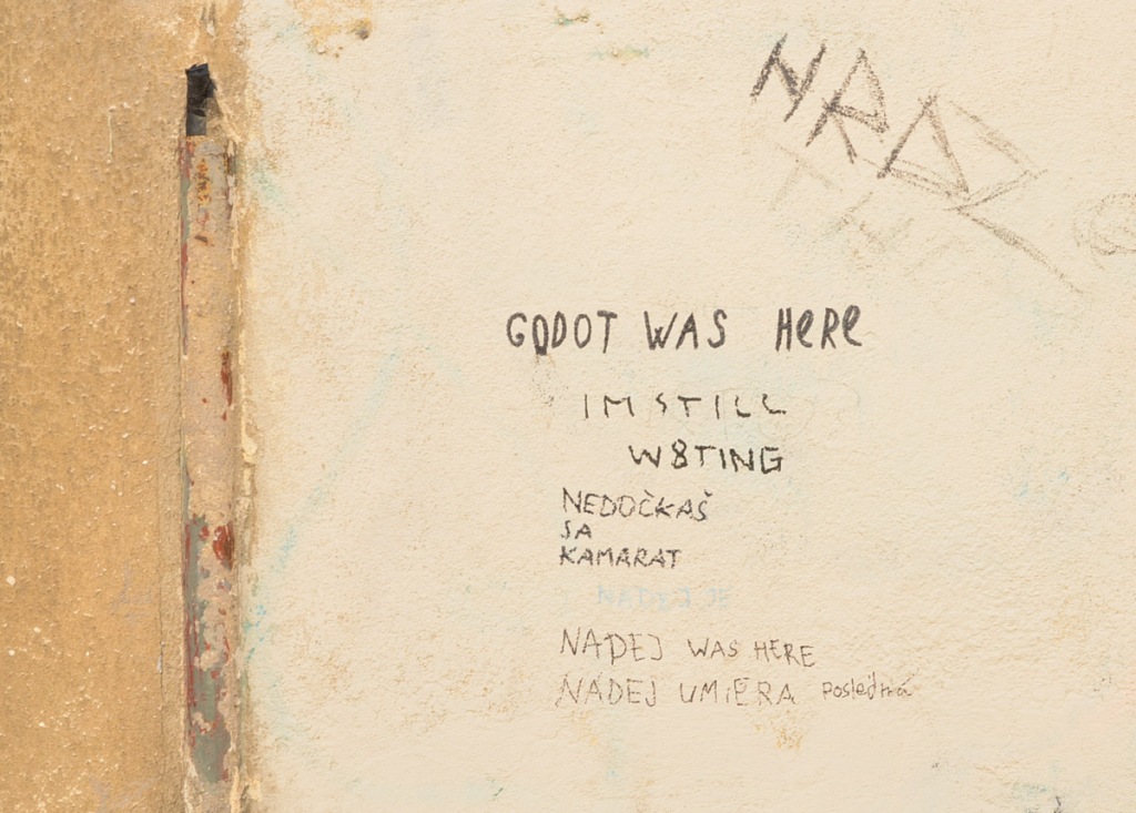 words written on a wall, by different people, including Godot was here, I'm still waiting, some words in Slovak, as well as was here 