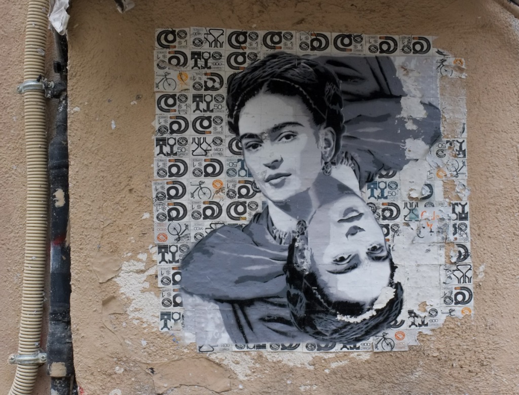 paper wheatpaste graffiti on a wall in Paris, looks like picture is printed on background of Mexican export stamps, or Mexican postage stamps.  Frieda Kahlo
s portrait, 2 copies, radially symmetrical, in grey tones, smiling, hair tied back