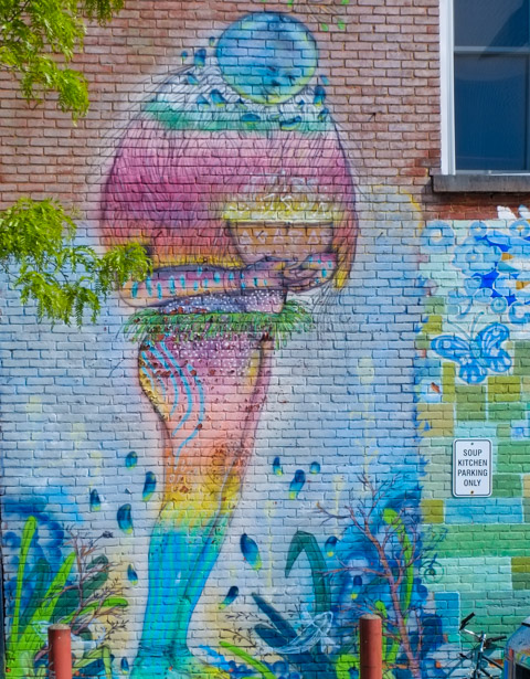 mural on the side of a wall, a character with round blue head holding a large bowl of food
