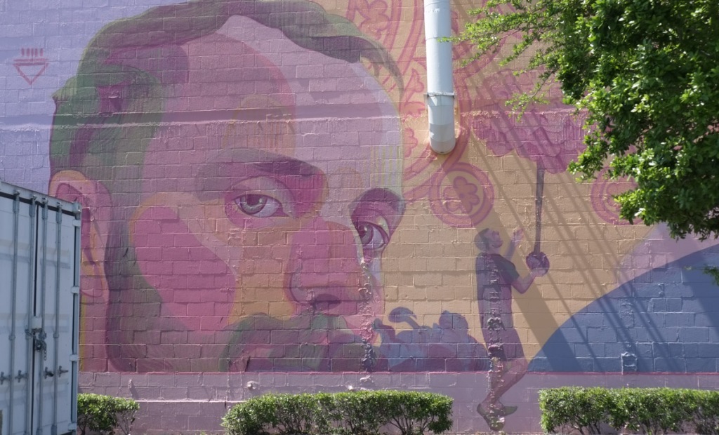 part of a mural, a man balancing a large pink flower by the bottom of its stem, a large man's face