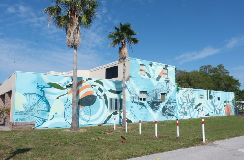 mural by  illsol, large, blue background, bicycles, oranges, locomotive, about history, orange belt railway, now on the pinellas trail in clearwater
