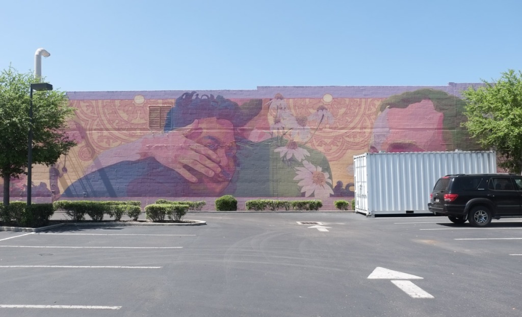 at the end of a parking lot in st petersburg, one black vehicle, one large white container, a mural with men's faces by gleo